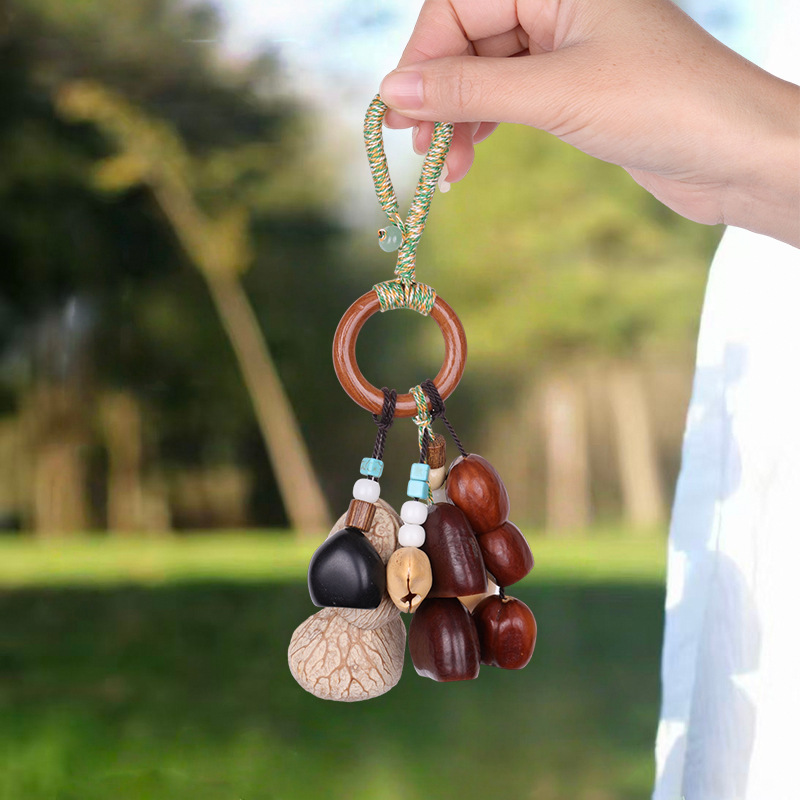 Handcrafted natural seed pod charm featuring a wooden ring wrapped in green thread, dangling various dark seeds, nuts, and a small green tassel, unique boho-style hanging accessory.