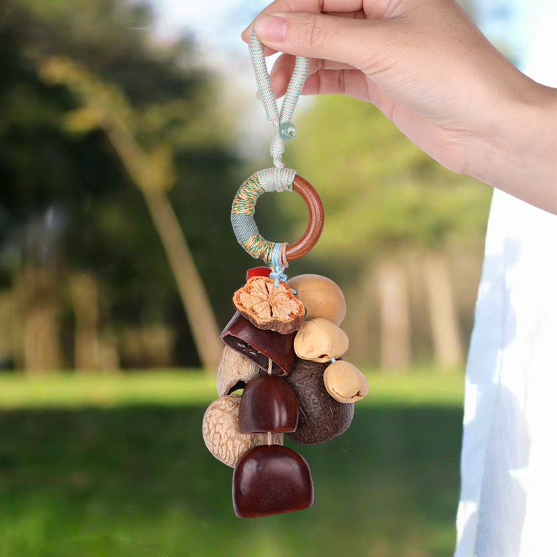 Handcrafted natural wind chime featuring a hand holding a unique arrangement of a large dried citrus slice, chestnuts, various tree nuts, and a decorative round brown ring hanging on a woven cord, organic boho-style home decor.