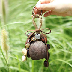 Product photography of a finished handcrafted natural fruit shell wind chime and shaker hanging charm held by a hand in an outdoor setting, with a small metal tag that reads "follow Your dreams.