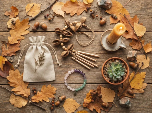 A product flat lay featuring natural, eco-friendly gift items—a seed pod wind chime, crystal bracelet, lit beeswax candle, and small succulent—arranged on a wooden surface covered in autumn leaves.