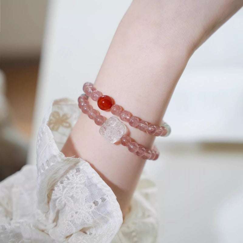 Handmade red string crystal bracelet worn on a wrist, combining protective cords with strawberry quartz for emotional healing.