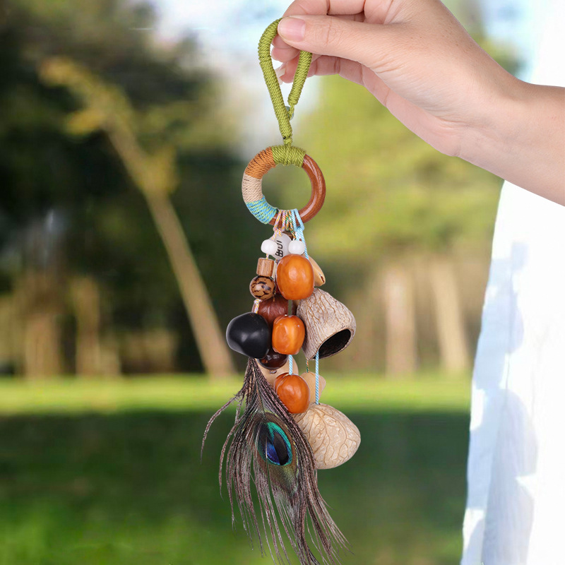 Handcrafted natural seed pod charm featuring a wooden ring wrapped in green thread, dangling various dark seeds, nuts, and a small green tassel, unique boho-style hanging accessory.